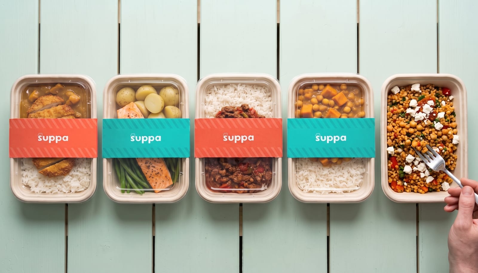 Five Suppa meals in a row on a mint table, four lidded in coral and teal sleeves, one open with a fork in it